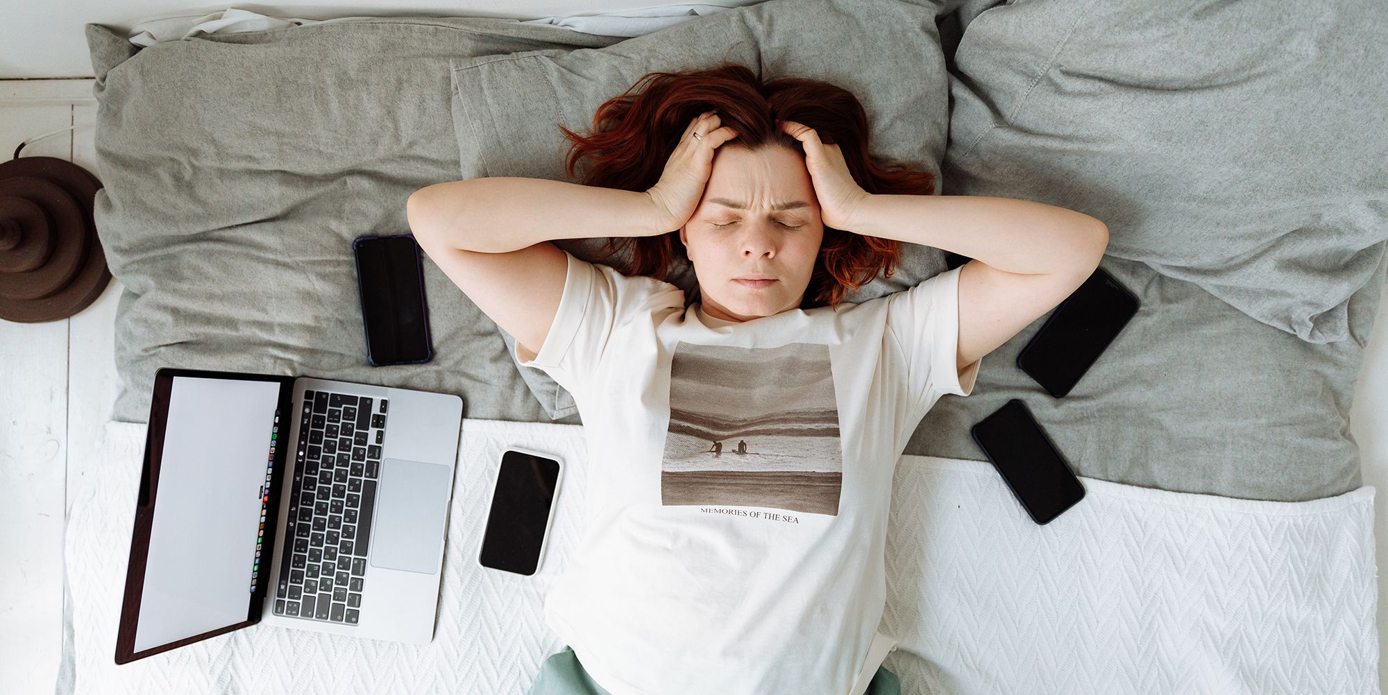 Wanita berbaring di tempat tidur frustrasi dengan laptop