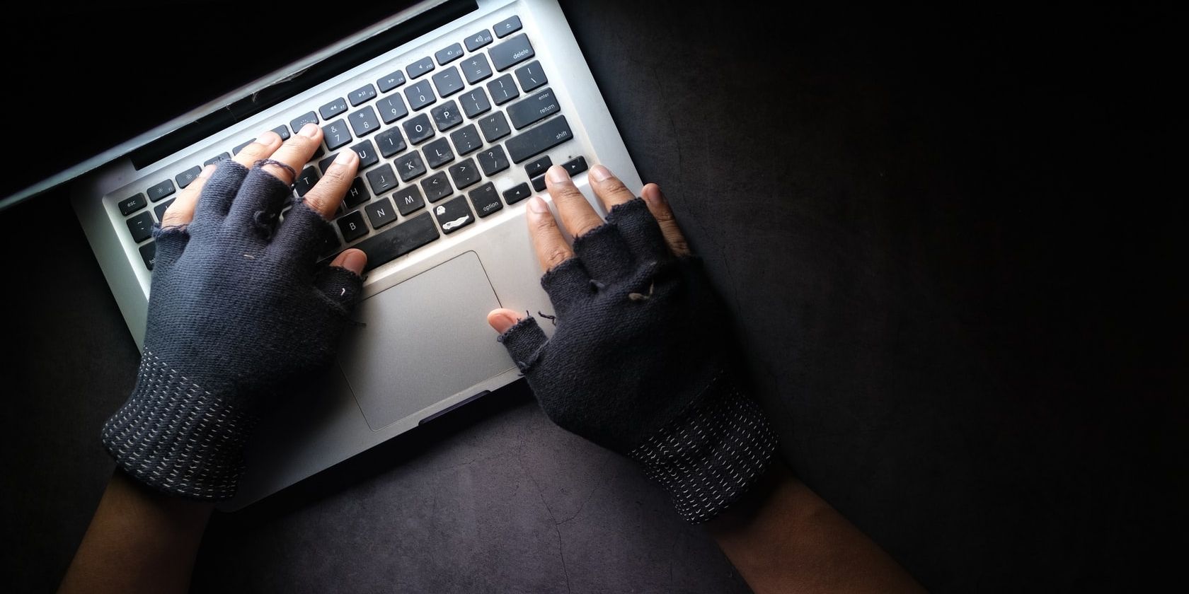 Buka MacBook di atas meja di ruangan gelap dengan mengetik tangan di sarung tangan tanpa jari hitam.